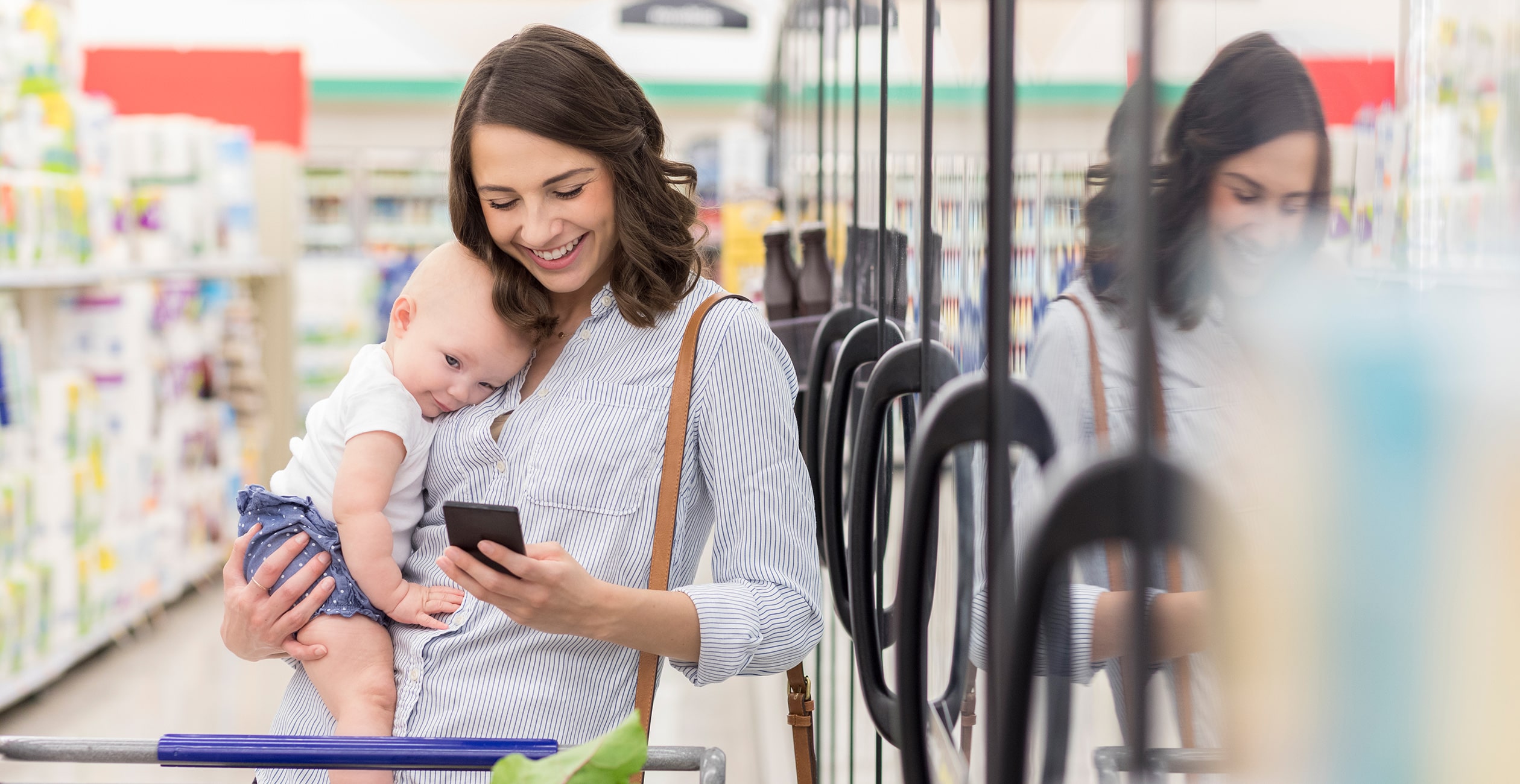 Woman holding her baby and a smartphone in a grocery store