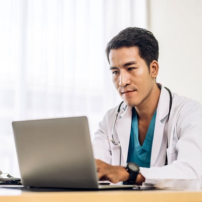 Asian-man-doctor-wearing-uniform-with-stethoscope-working-with-laptop-computer-in-hospital