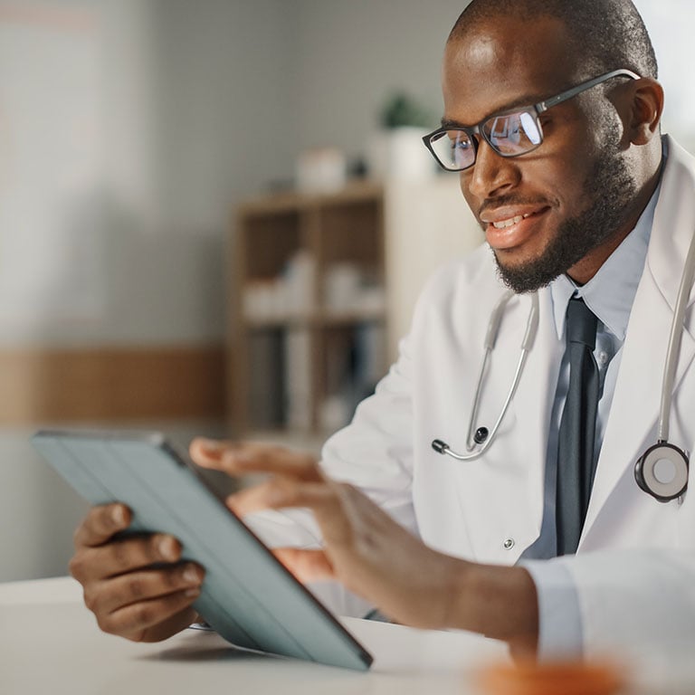 Happy-and-Smiling-African-American-Male-Doctor-Wearing-White-Coat-Working-on-Tablet-Computer-at-His-Office