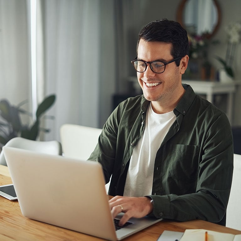 Happy man wearing eyeglasses using laptop at home