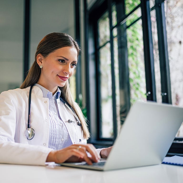Positive-doctor-working-on-laptop-in-medical-office,-portrait.