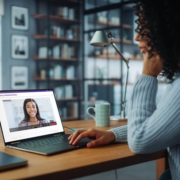 A woman talks with her physician virtually on a laptop