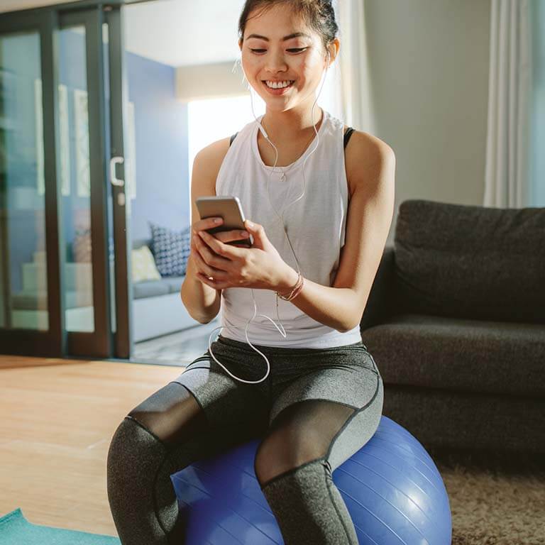 A young woman balances on an exercise ball while looking at her phone
