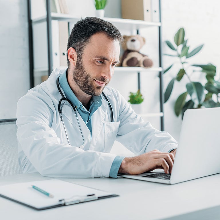 smiling doctor sitting at desk and using laptop